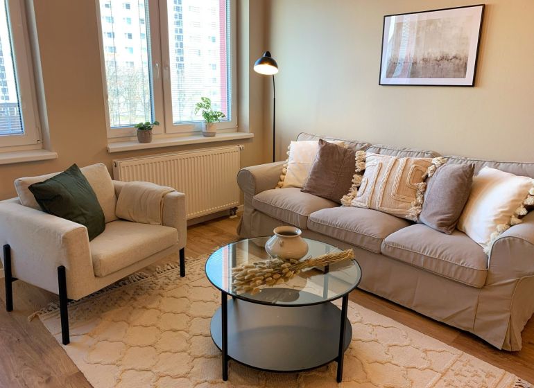 Living room in a 2-room apartment with a gray sofa, an armchair, and a wooden decor floor.