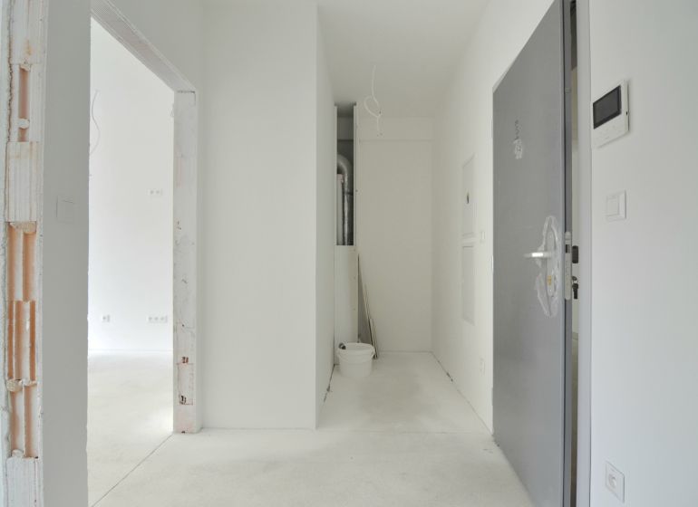 A hallway in a 2-room apartment with a concrete floor and open doors.