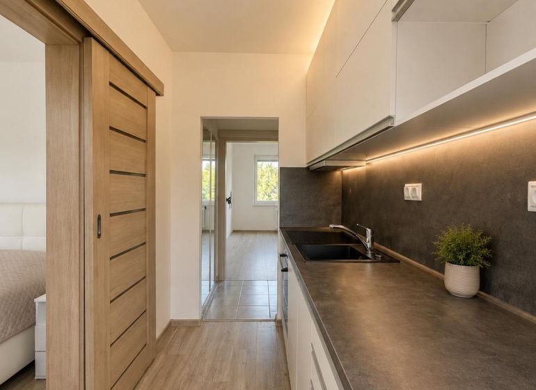 A kitchen in a 2-room apartment with a wooden decor floor and sliding doors.