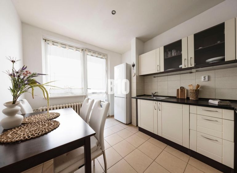 A kitchen in a 3-room apartment with a dining table, white cabinets, and a large window.