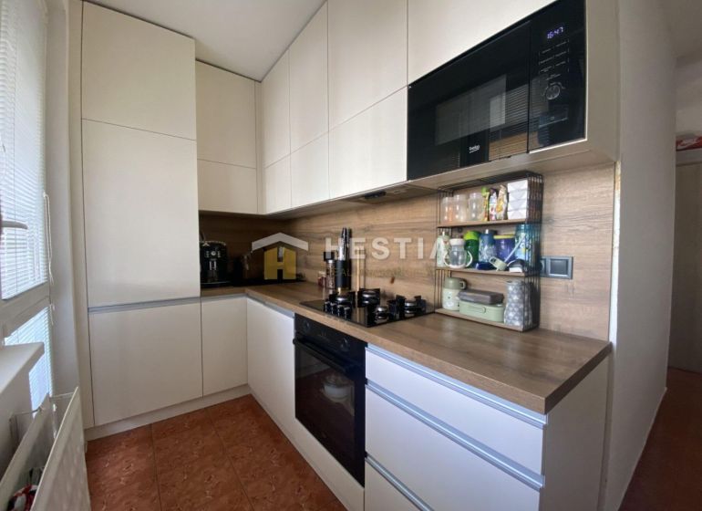 A kitchen in a 2-room apartment with white cabinets and a wooden decor.