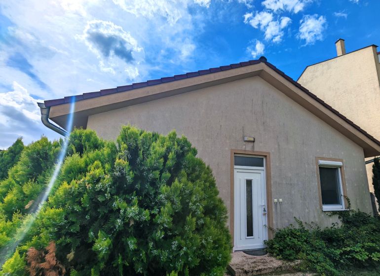 A family house in Matúškovo with white doors, surrounded by greenery under a sunny sky.