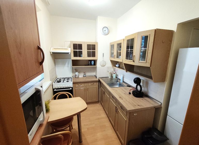 A kitchen in a studio apartment with a wooden decor floor, table, chairs, appliances.