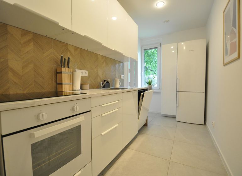 A kitchen in a 2-room apartment with white cabinets and a backsplash with a wooden decor.