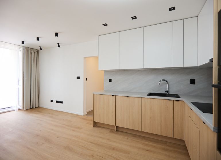 A kitchen space in a 2-room apartment with a wooden decor floor and white cabinets.
