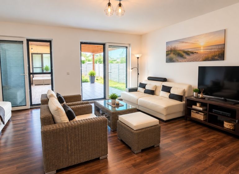 A bright living room with wood-patterned flooring, white sofas, and rattan furniture.