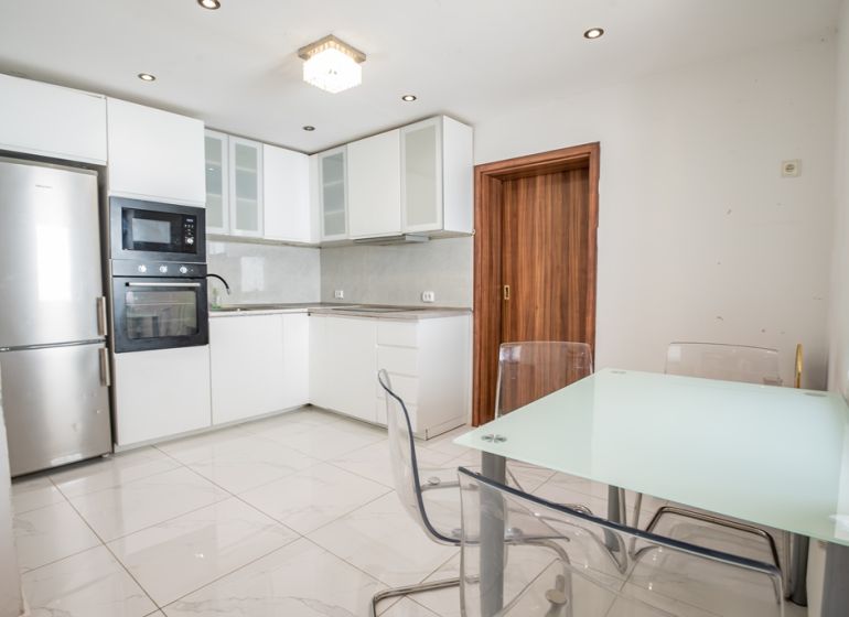 A kitchen in a family house with a glass table, cabinets, and appliances, flooring with a white decor.