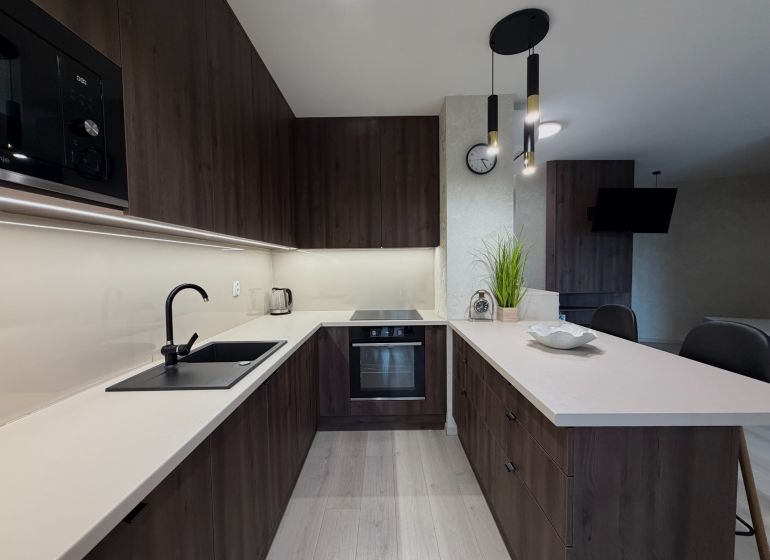 A kitchen in a 2-room apartment with dark furniture and a wooden decor floor.