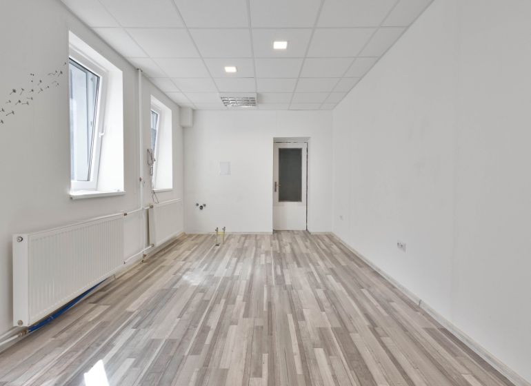 Empty commercial space with wood-patterned flooring and two windows.