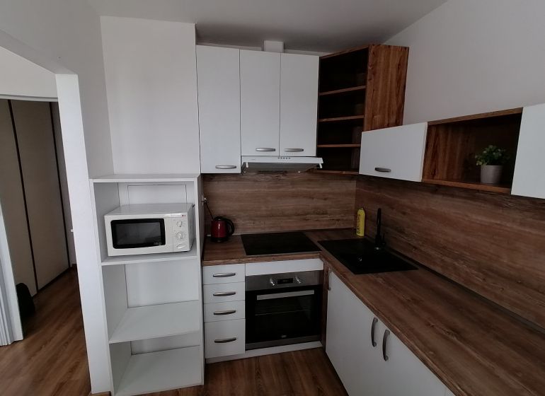 A kitchen with white cabinets and appliances in a studio apartment; floor with wood decor.