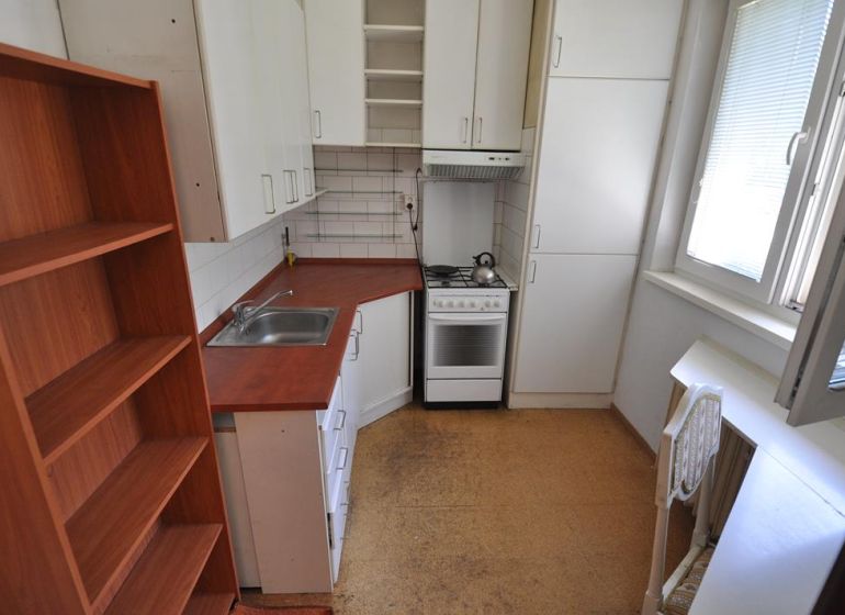 A kitchen in a three-room apartment, with a stove, cabinets, and a floor with a wood decor.