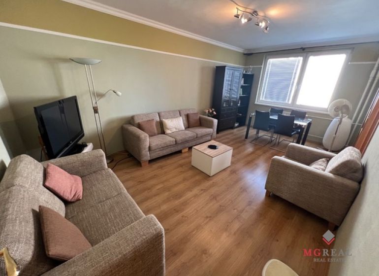 Living room with wood-patterned flooring, sofas, and a coffee table in a three-room apartment.