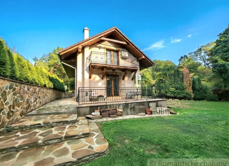A cottage in Ružiná with a stone staircase and a lawn surrounded by greenery and a blue sky.