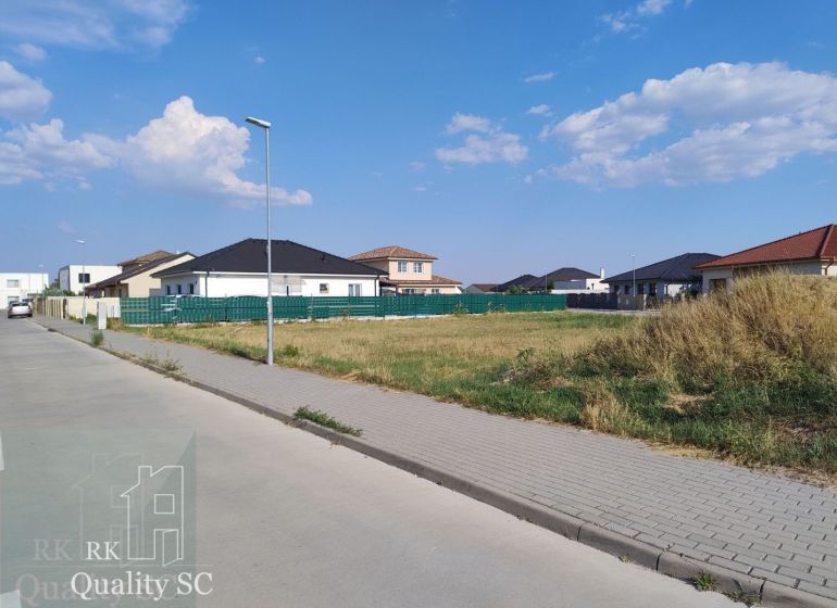 Residential plots in Senec surrounded by houses and greenery under a blue sky.