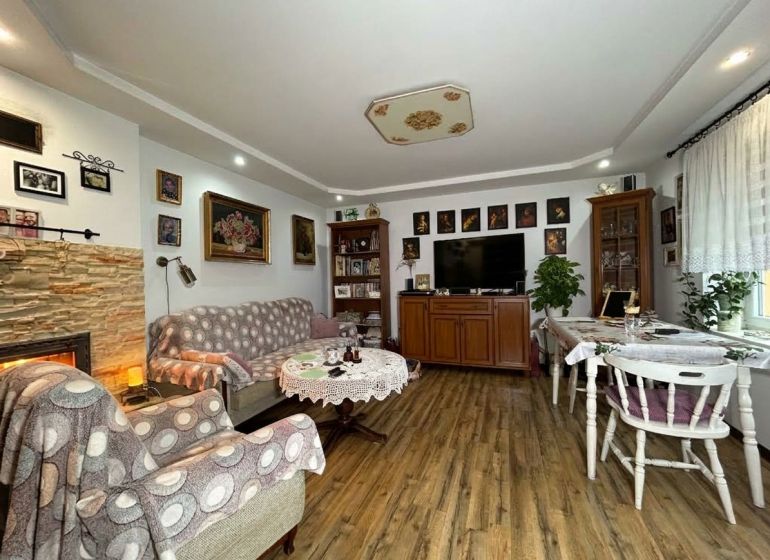 Living room with wood-patterned flooring in a two-room apartment, decorated with paintings and a fireplace.