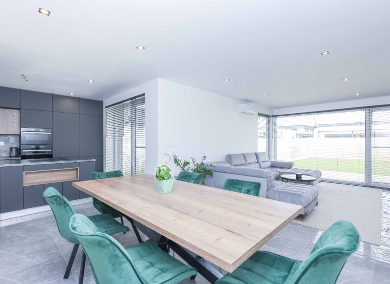 A family house with a kitchenette, a gray sofa, green chairs, and a wooden-patterned floor.