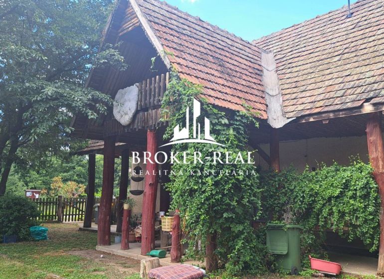 A cottage in Abaújkér surrounded by greenery with a traditional sloped roof and wooden columns.