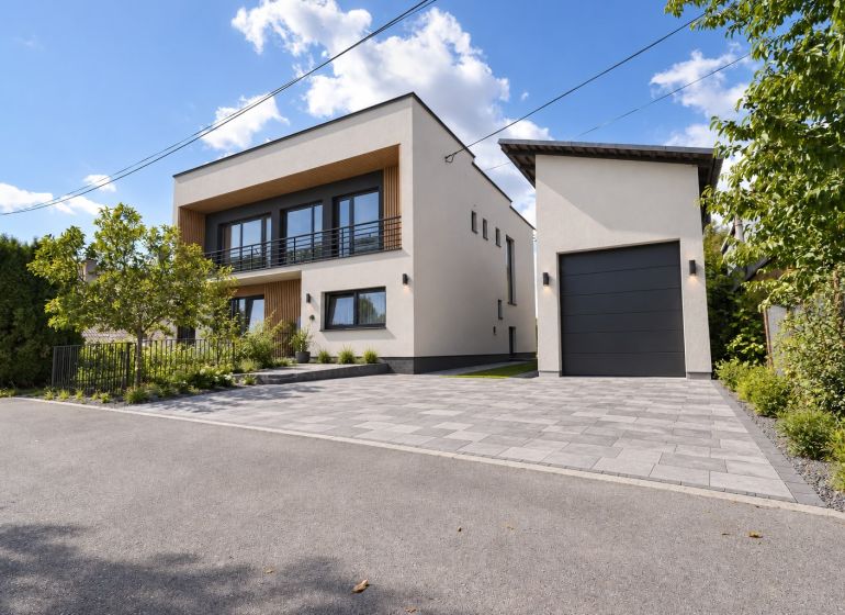 A family house in Badín with a two-story white facade and a garage surrounded by greenery.