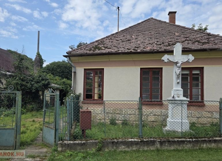 A family house in Boldogkőújfalu with a simple facade and a stone cross in the garden.