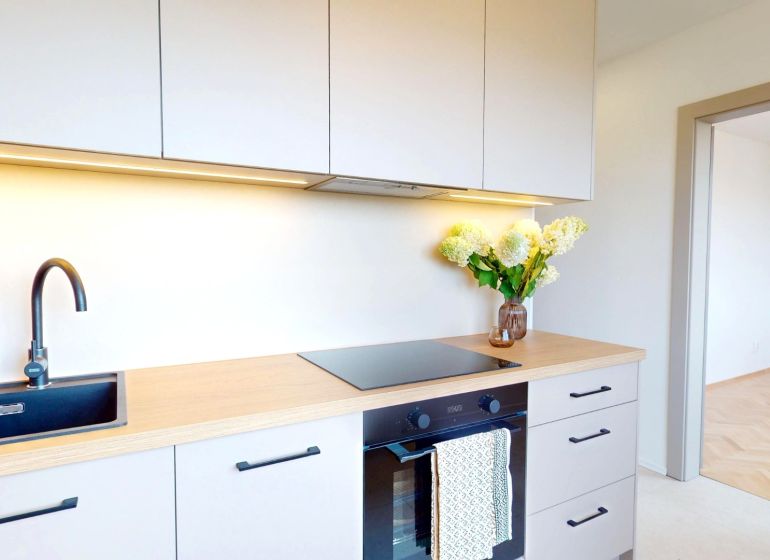 A kitchen in a 3-room apartment with a cooktop, a black sink, and flowers on the counter.