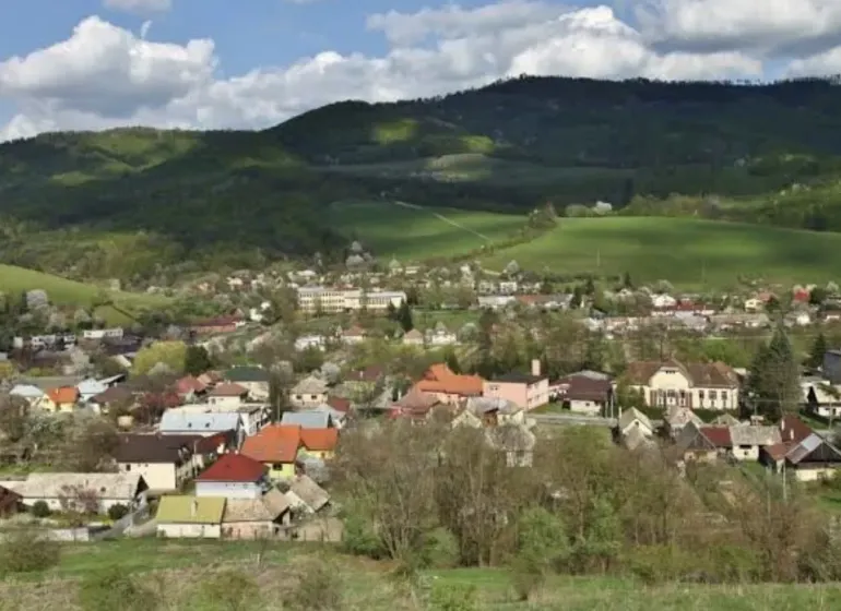 A view of Kokava nad Rimavicou surrounded by hilly landscape and gardens.
