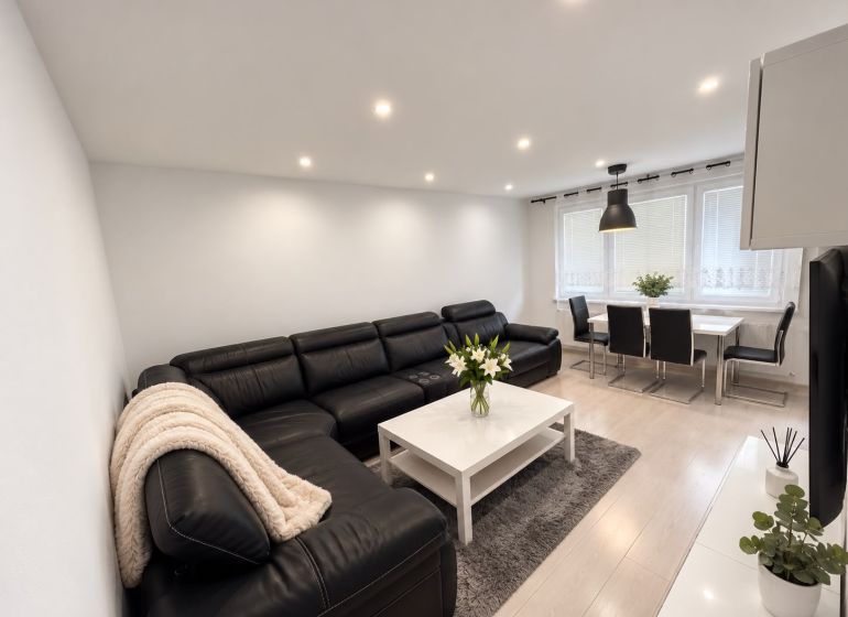 Living room of a 3-room apartment with a leather sofa, dining table, and wooden decor flooring.