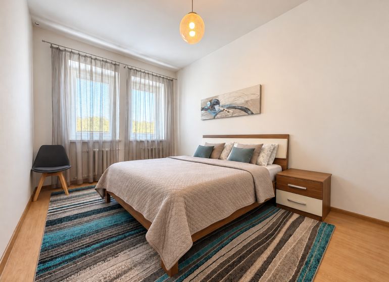 A bedroom in a 3-room apartment with a bed, an armchair, and a floor with a wooden decor.