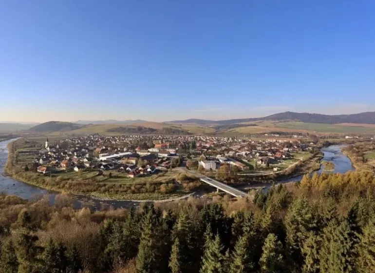 Panorama of agricultural and forest lands in Plavča with a river and a bridge in the background of the forest.