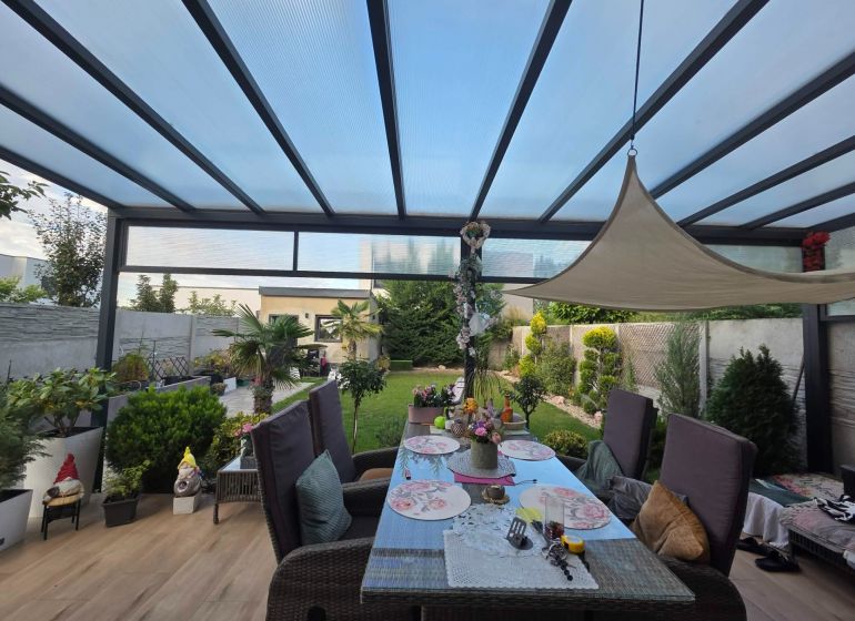 A covered terrace with a dining table and a view of the garden in a family house.