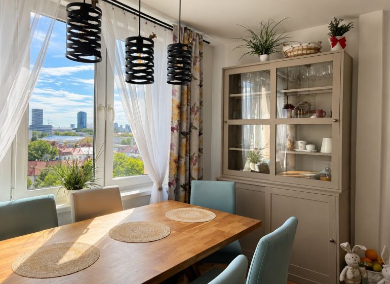 Dining area with a wooden table and a view in a 3-room apartment with plants.