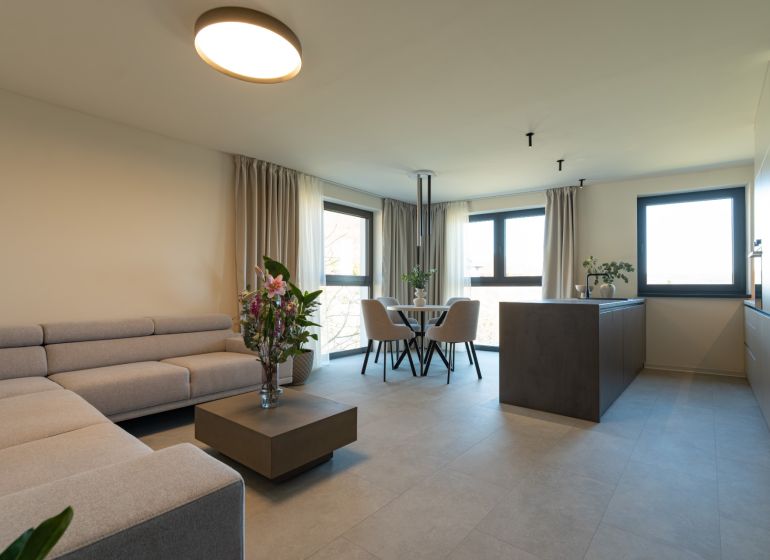 Living room with a sofa, flowers, dining table, and kitchen island in a 4-room apartment.