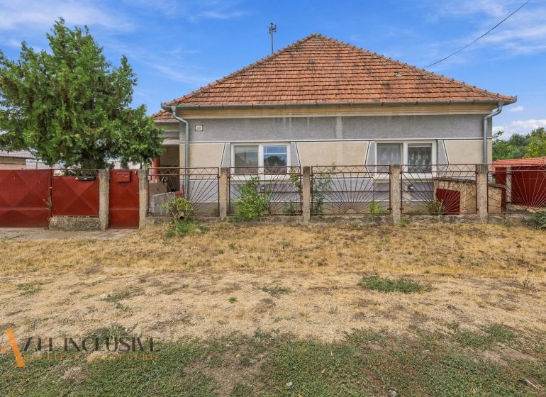 A family house in Bátorove Kosihy with a red roof and fence. Dried lawn.
