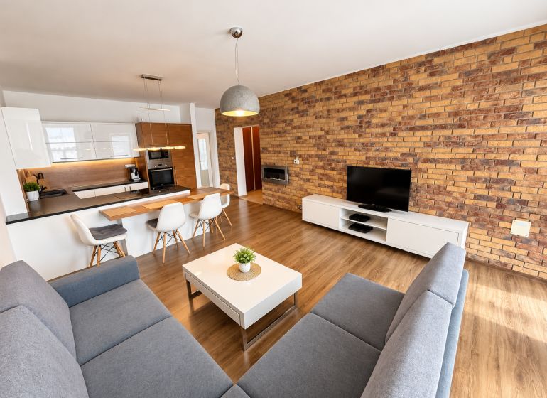 Living room of a two-room apartment with a wooden decor floor and a brick wall.