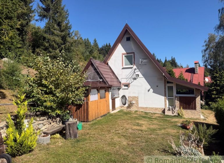A cottage in the village of Látky surrounded by green trees and a manicured lawn.