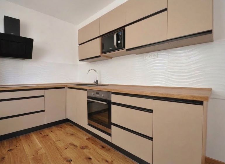 A kitchen in a 2-room apartment with a wooden decor floor and light cabinets.