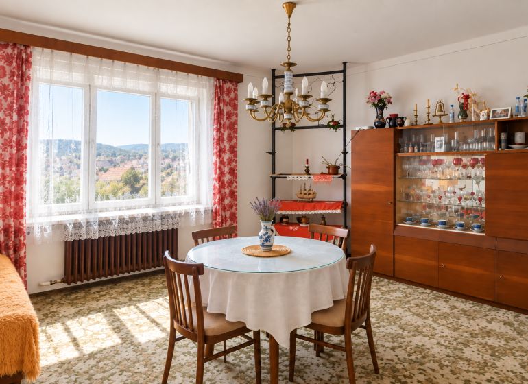 A dining room in a family house with floral curtains and a glass cabinet.