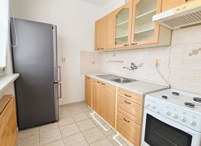 A kitchen in a studio apartment with a refrigerator, stove, and light-colored furniture.