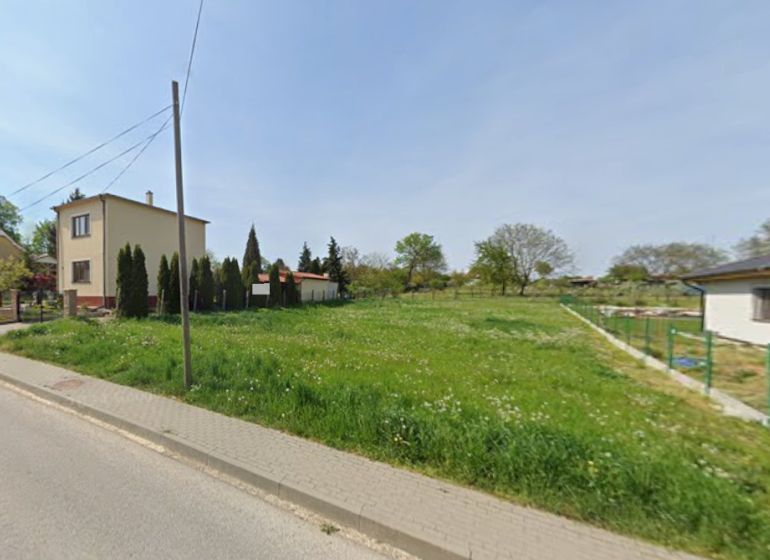 A green residential plot in the village of Bardoňovo, bordered by family houses.