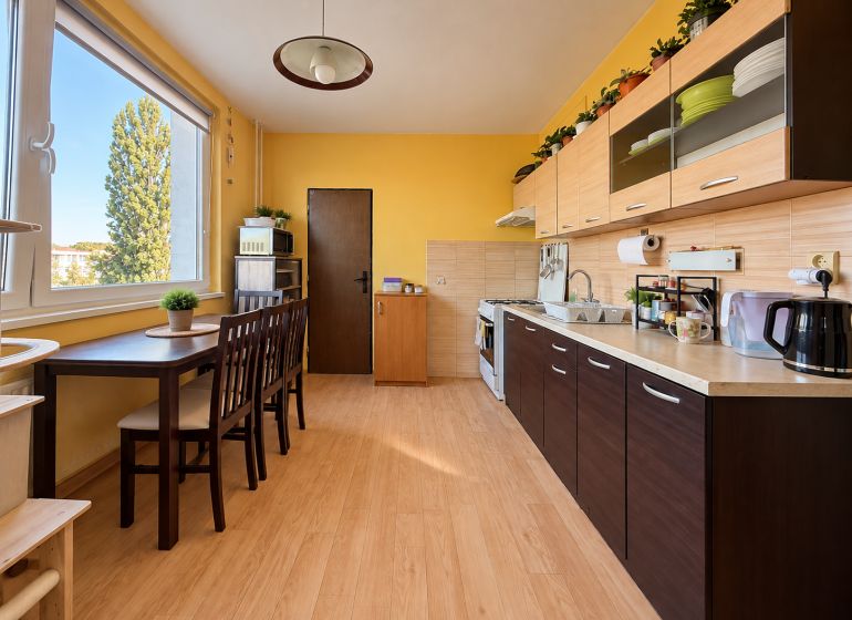 A kitchen in a 2-room apartment with a wooden decor floor and yellow walls.