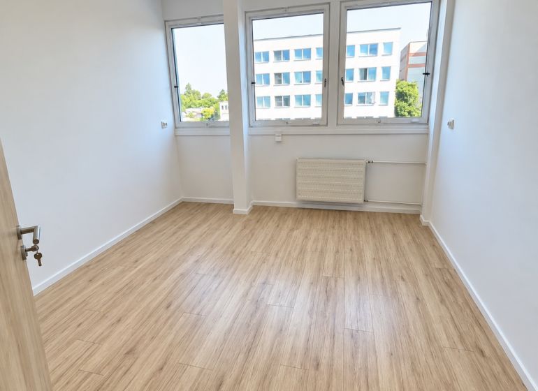 An office with a wooden floor design, interior with large windows and ceiling lighting.