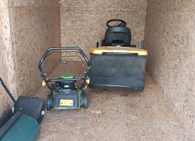 A wooden shelter with garden equipment including lawnmowers in the gardens.