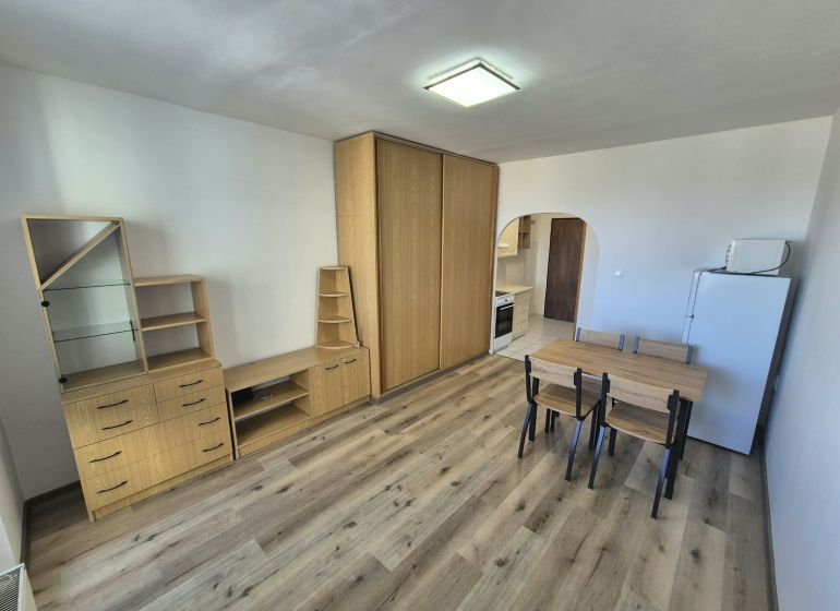 A studio apartment with a wooden floor, furniture, dining table, and kitchenette.