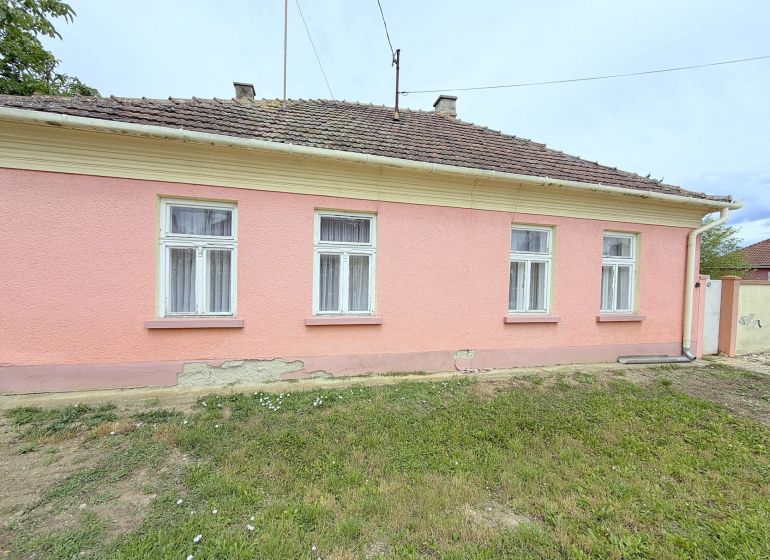 A family house in Dunakiliti with a pink facade and four windows on the ground floor.