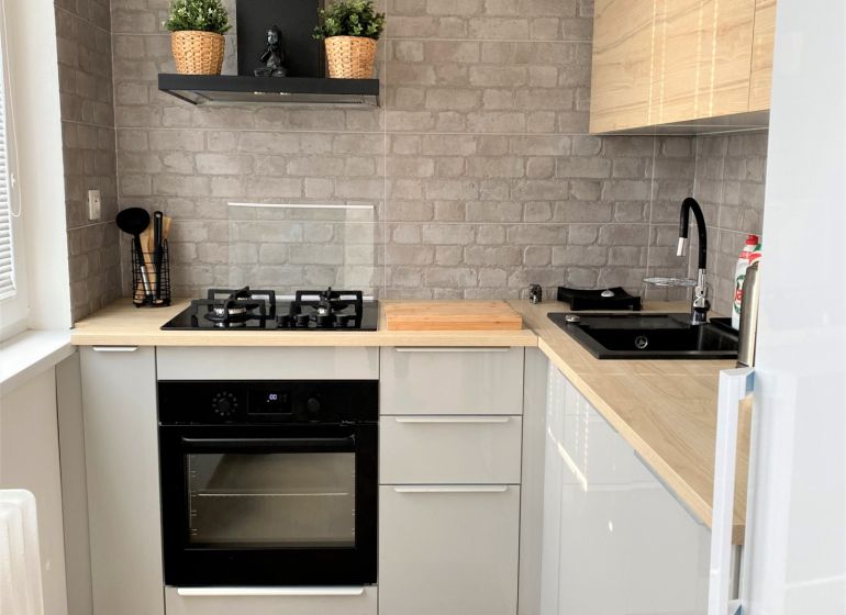 Compact kitchen in a 3-room apartment with a stove, sink, and gray brick tiles.