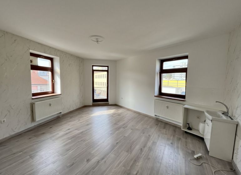 A room with windows, white walls, a wood-patterned floor, and a sink in the office.