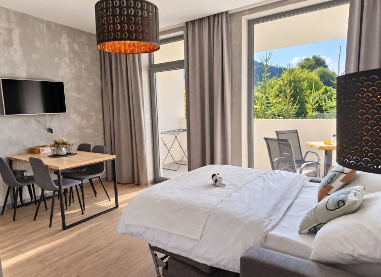 A room in a 2-room apartment with a wooden decor floor, a dining table, and a bed.