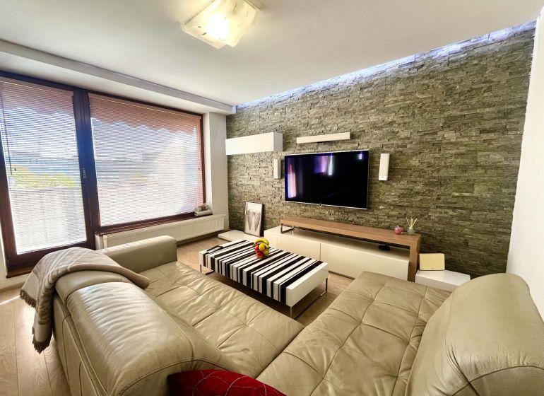 Living room in a 3-room apartment with a leather sofa, stone wall, and floor with a wooden decor.