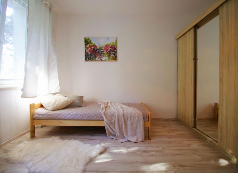 A studio apartment with a simple bed, a wardrobe, and a floor with a wooden decor.