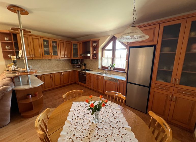 A family house kitchen with wooden furniture, a floor with a wooden design, and a dining table.