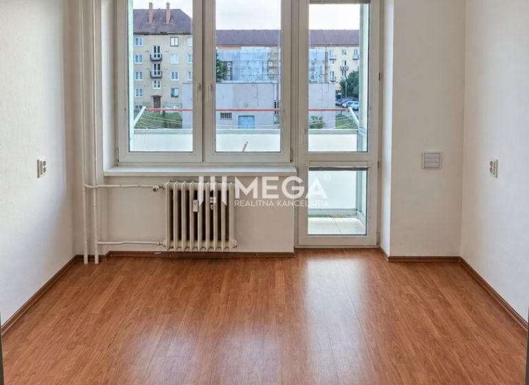 A room in a 2-room apartment with a wooden decor floor and a large window.